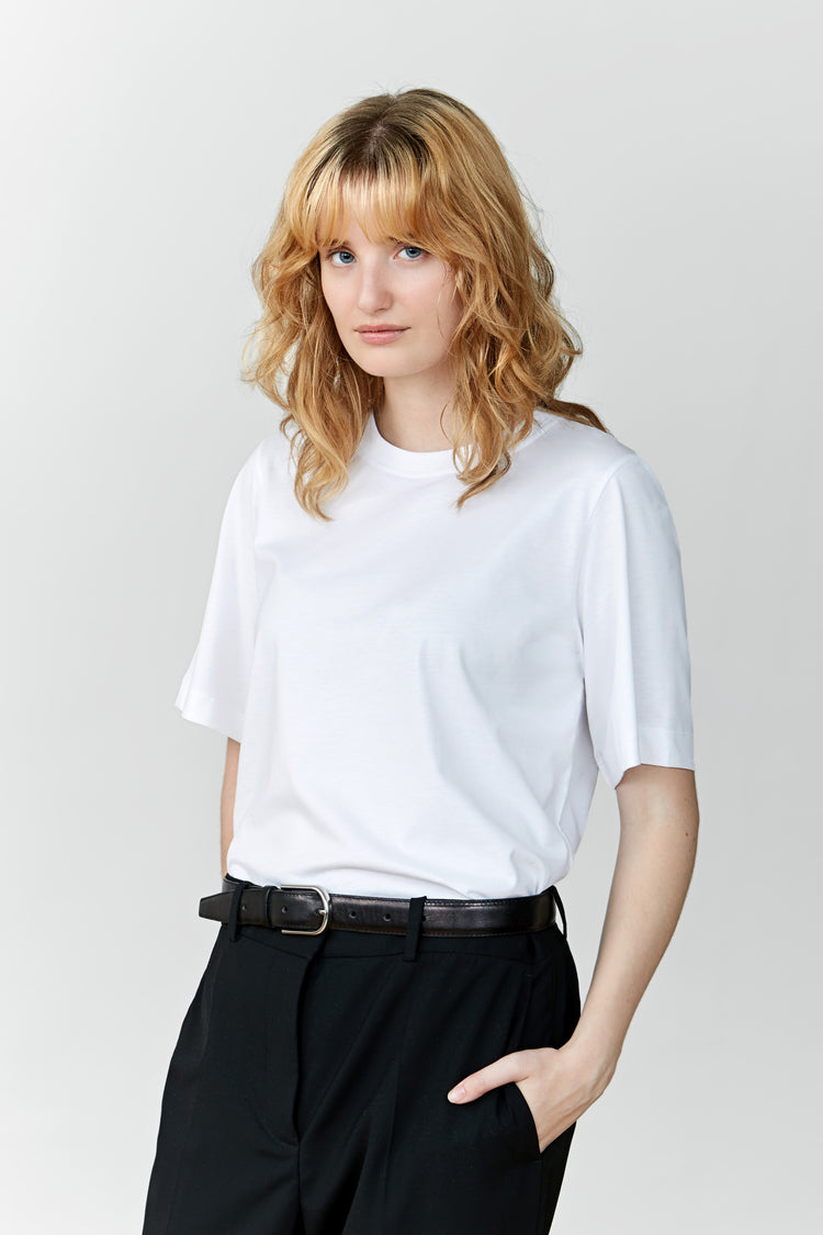 A woman wearing a white regular T-shirt with a classic crewneck tucked into black trousers.