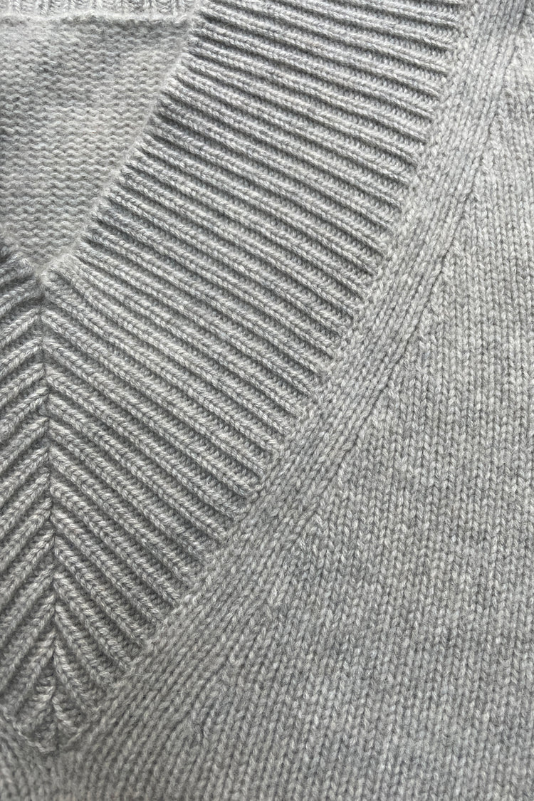 Detail of front neckline on a v-neck cashmere sweater in light grey photographed flat.
