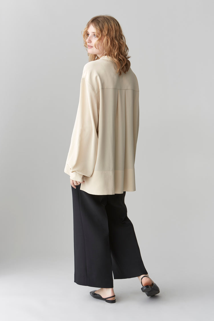 Side profile of HELEN oversized silk blouse showcasing the exaggerated stepped hem and relaxed silhouette.