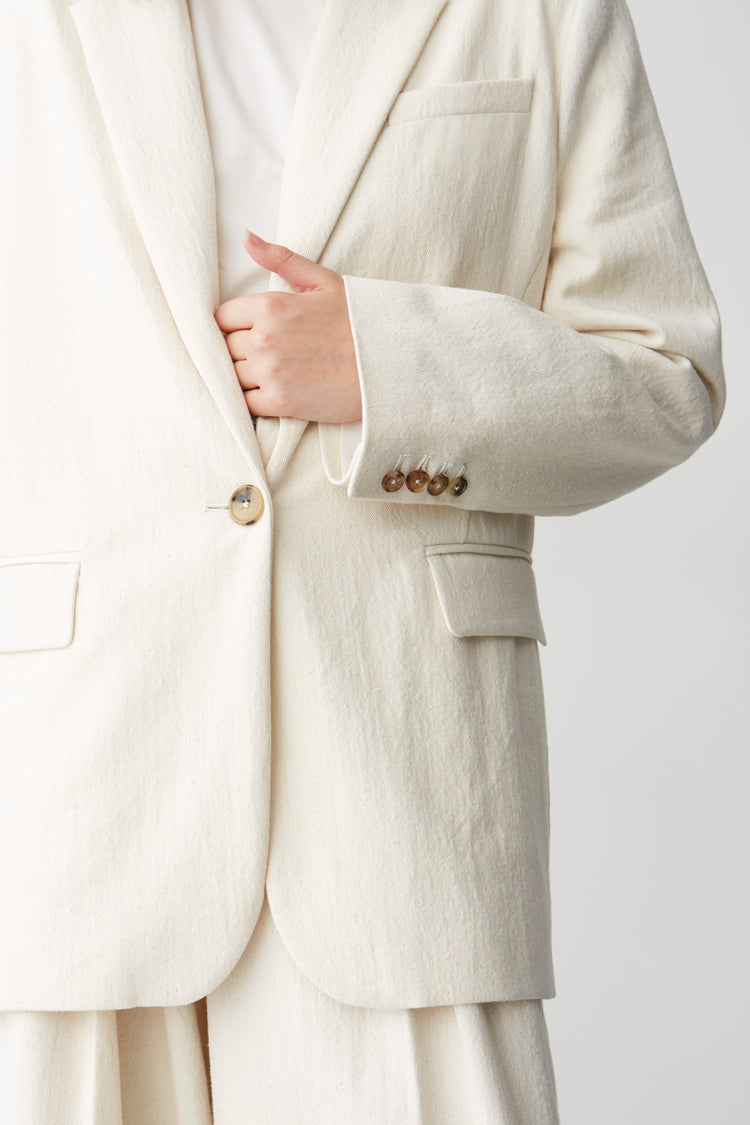 Details of a horn buttoned, cream-hued jacket sleeve with matching pants and a white T-shirt.