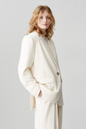 A cropped image of a woman wearing a horn-buttoned, cream-hued, single-breasted jacket styled as a suit with matching pants and a white T-shirt.