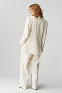 The back of a woman wearing a horn-buttoned, cream-hued jacket styled as a suit with matching pants.